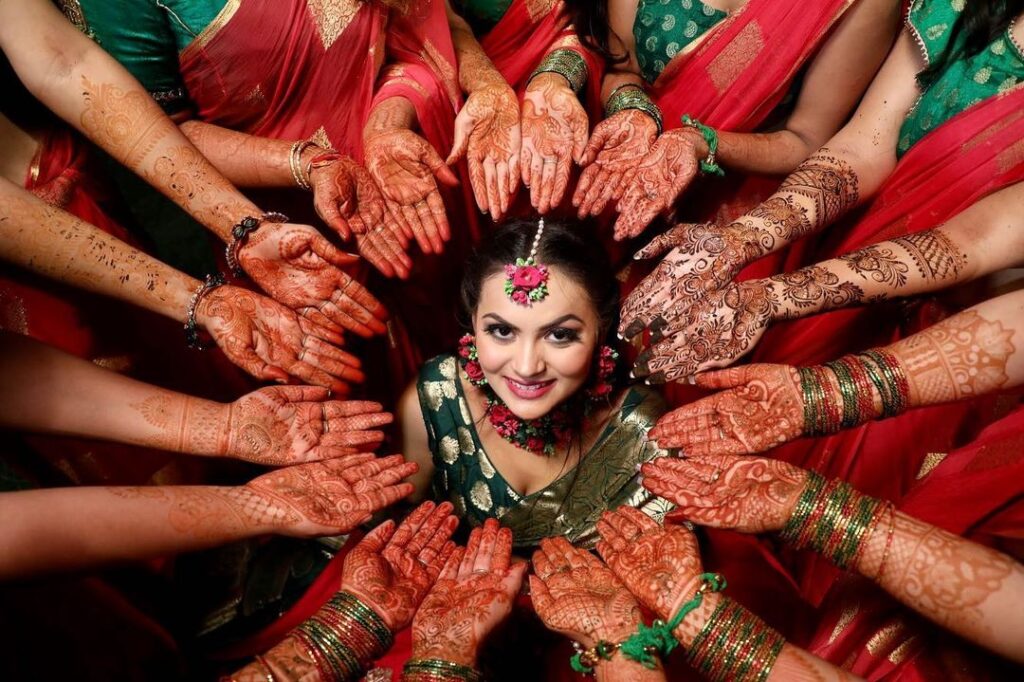 Bride with many family members hands with intricate Mehendi designs, set against a beautifully decorate by Gaur Wedding Decor.